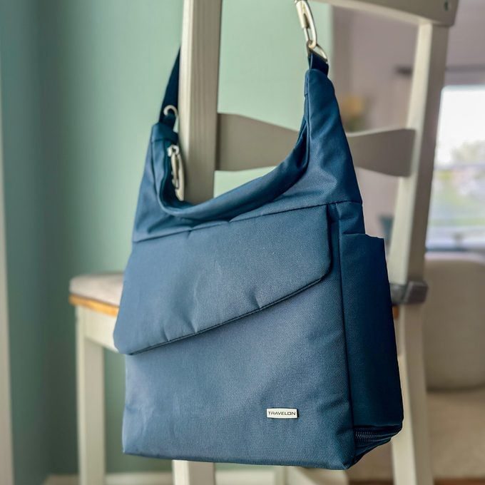 A blue shoulder bag hangs on a chair in a softly lit room. Label reads 
