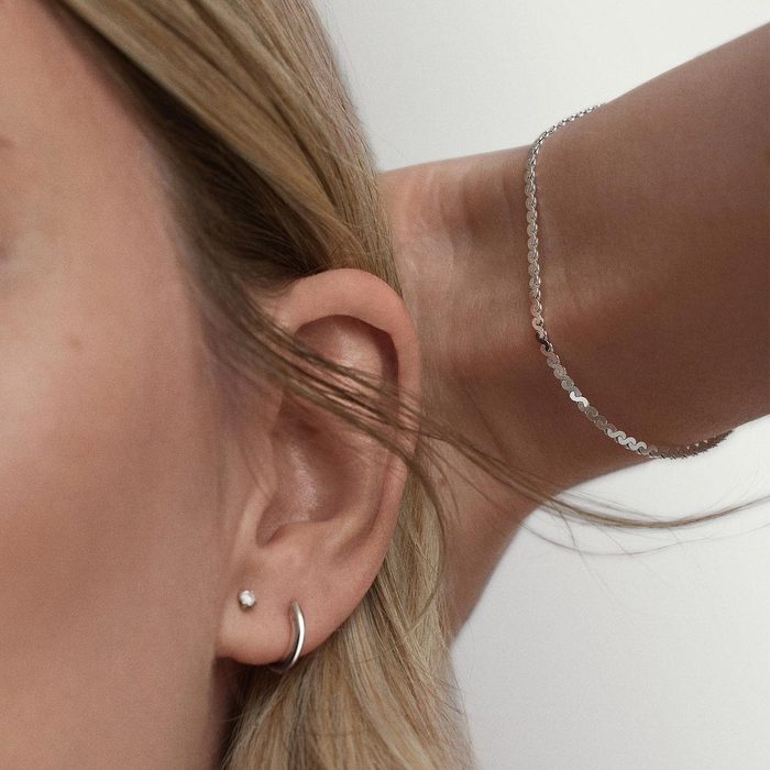 An ear adorned with a small earring; a wrist with a thin, silver bracelet is raised near the head, set against a neutral background.
