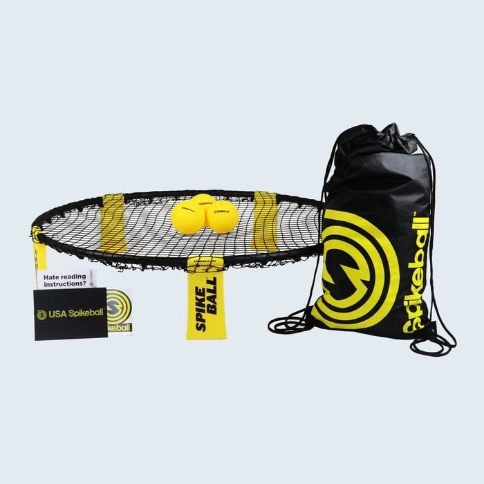 Round net holds two yellow balls, set beside a branded black drawstring bag and instruction booklet, in a Spikeball game setup.