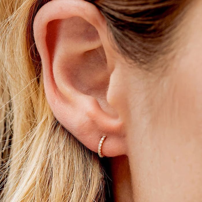 An ear displays a small, sparkling hoop earring; the ear is surrounded by light brown hair.