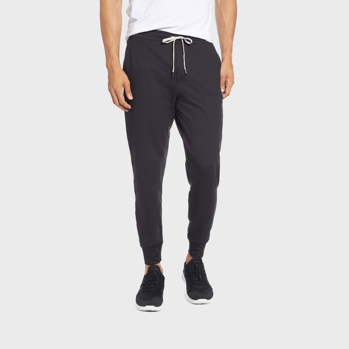 Man wearing black joggers and sneakers stands, showcasing casual attire in a neutral space.