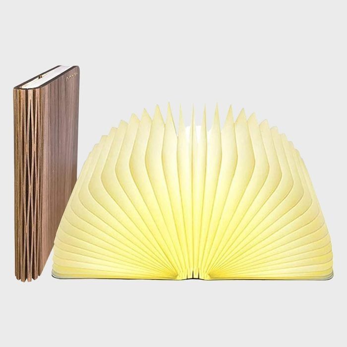 Book-shaped lamp emits yellow light; closed version stands upright beside it, in a plain gray setting.