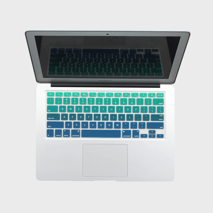 Laptop displays colorful silicone keyboard cover; seen from above, it spans various shades of green and blue, in a neutral indoor setting.