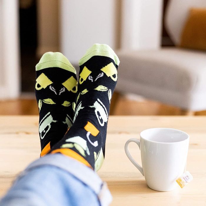 Socks with fun Halloween designs rest on a table; nearby, a white mug holds a teabag in a cozy, home setting.