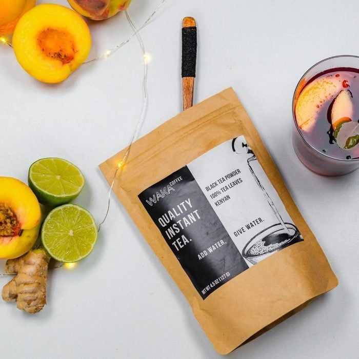 Tea package lies near sliced fruits and a glass of tea on a table. Text: 