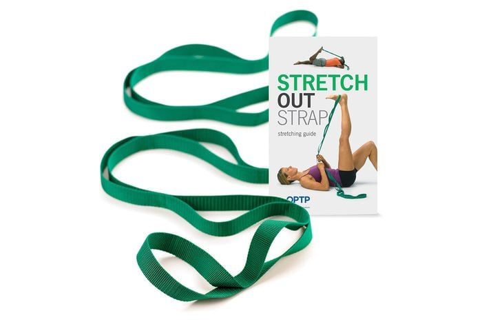 Green stretching strap lies extended next to a leaflet showing a person using it for leg exercises. Text includes 