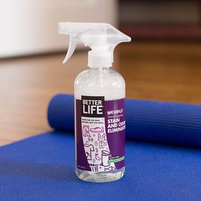 A spray bottle rests on a blue yoga mat indoors, labeled 