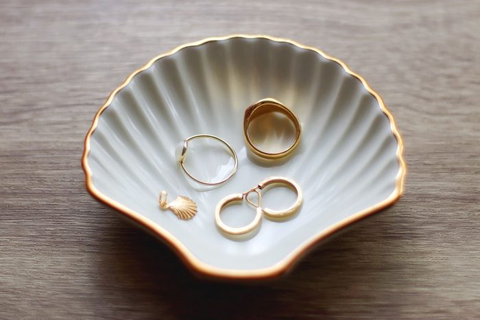 Ring dish shaped like a seashell with gold rings, earrings and pendant. Wooden background, selective focus.