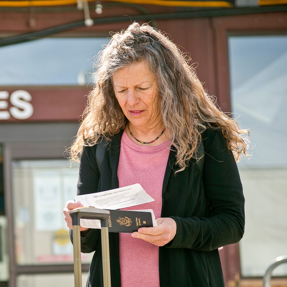 A woman looks at her paper boarding passes with her U.S. passport in front of a departure door