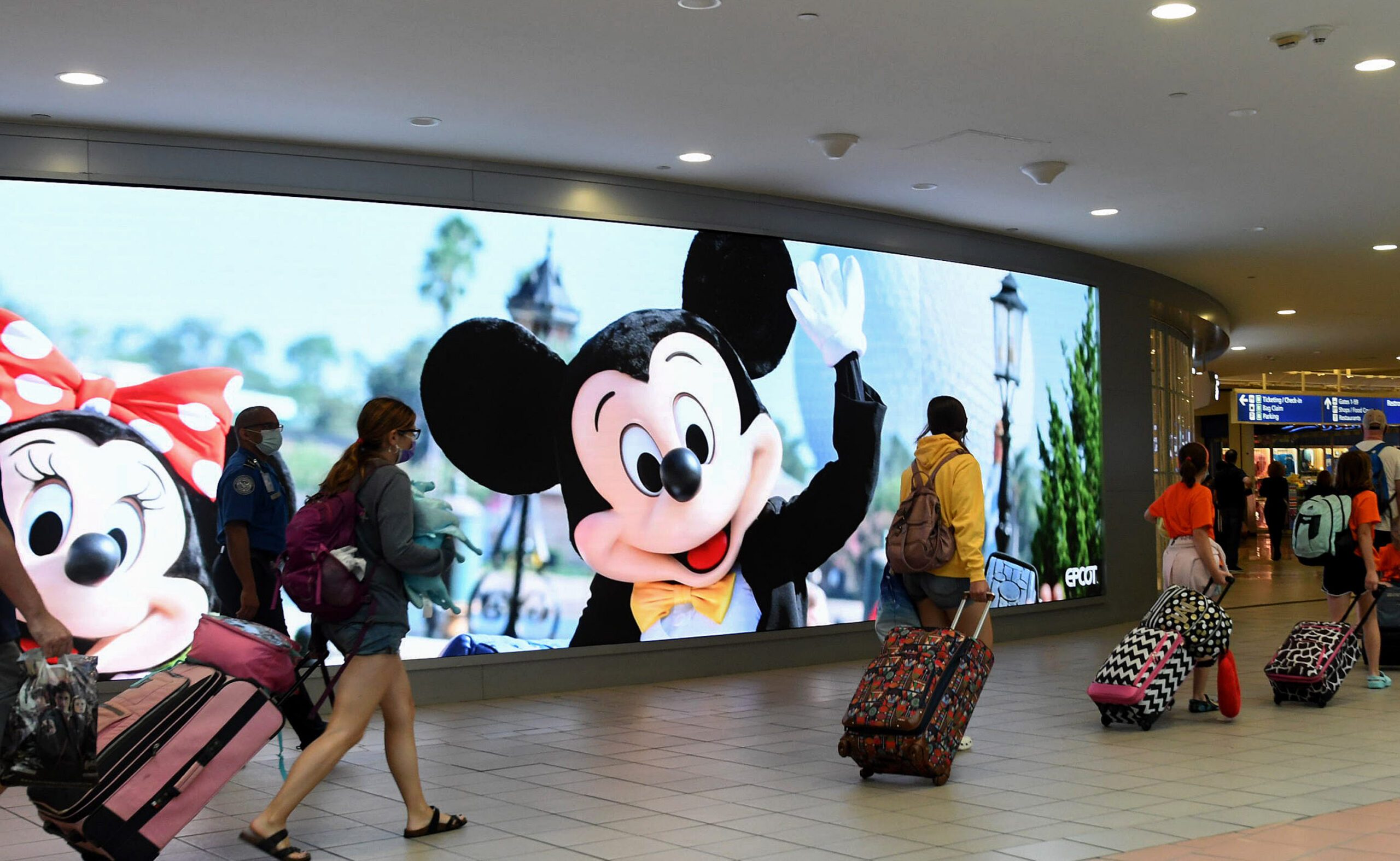 Travelers walk past a sign advertising Walt Disney World at Orlando Airport