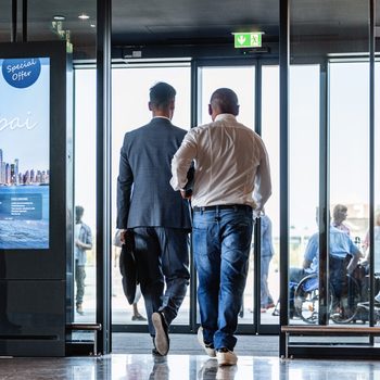 Two men exit through glass doors at an airport