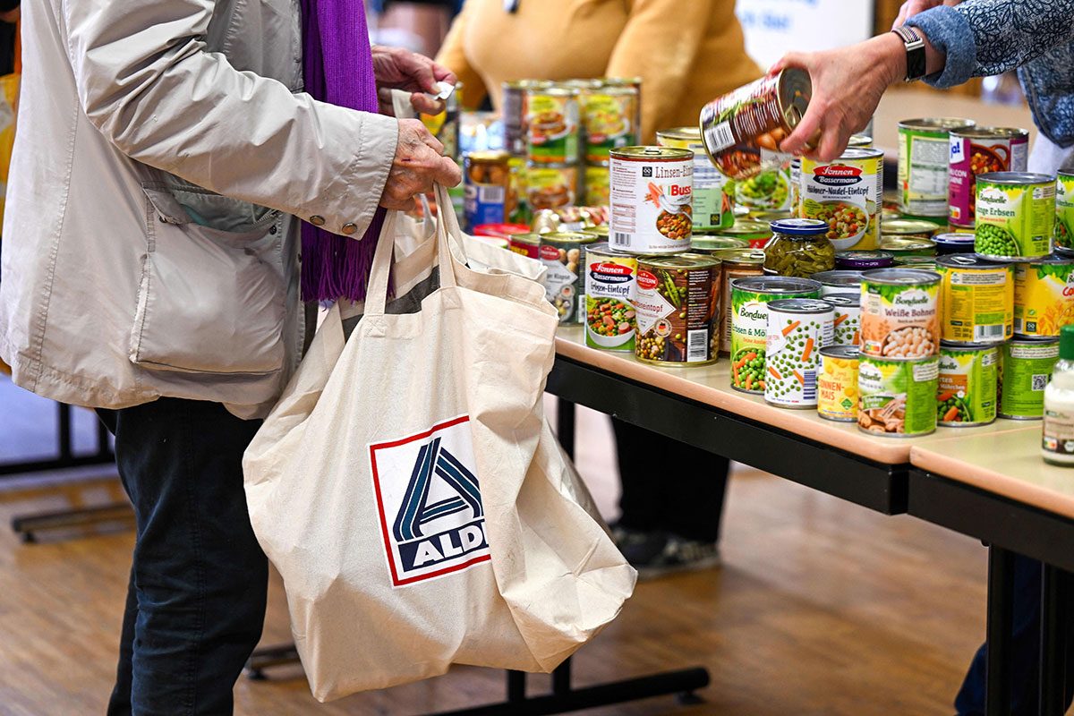 A volunteer hands a food tin can to a customer who holds a bag by Aldi supermarket chain at a food bank