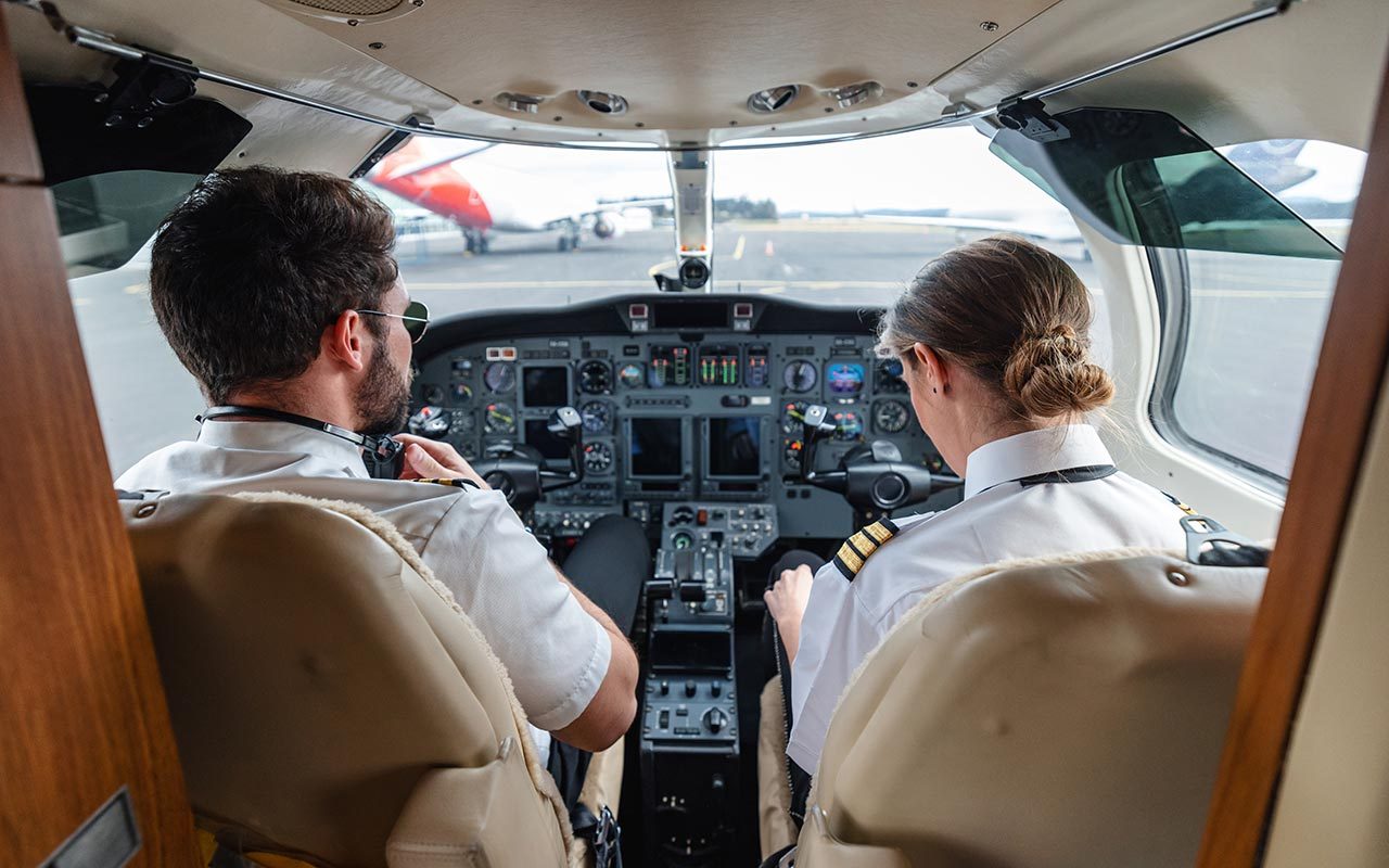 Male and female pilots in aircraft cockpit, checking systems before takeoff for a business travel flight.
