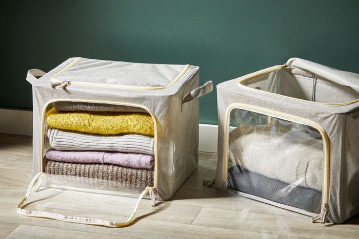 Seasonal storage bins with sweaters. One bin is open on top, the other is open on the clear window side
