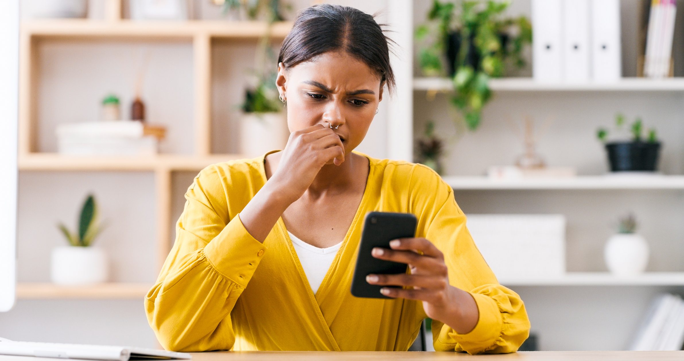 Woman in yellow cardigan with a concerned look on her face looking at her smartphone